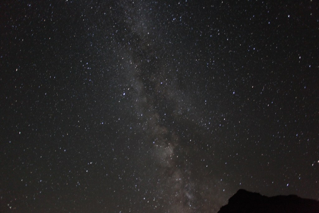 Una vista notturna della Via Lattea illuminata da numerose stelle, con una silhouette di montagne in basso.