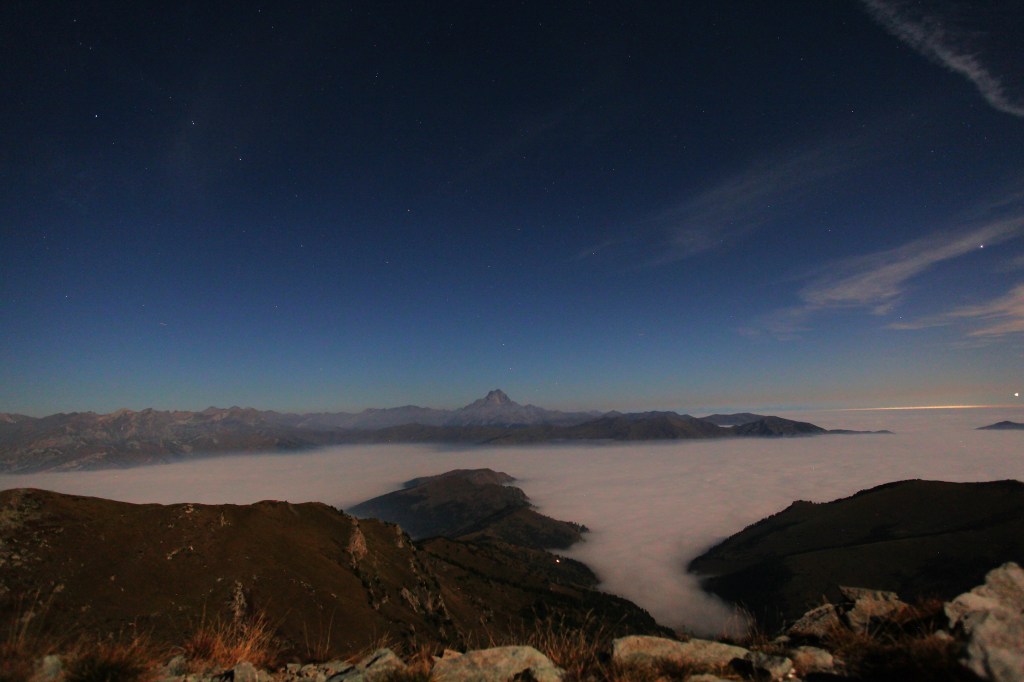 Vista notturna delle montagne sopra una fitta coltre di nebbia, con un cielo stellato.